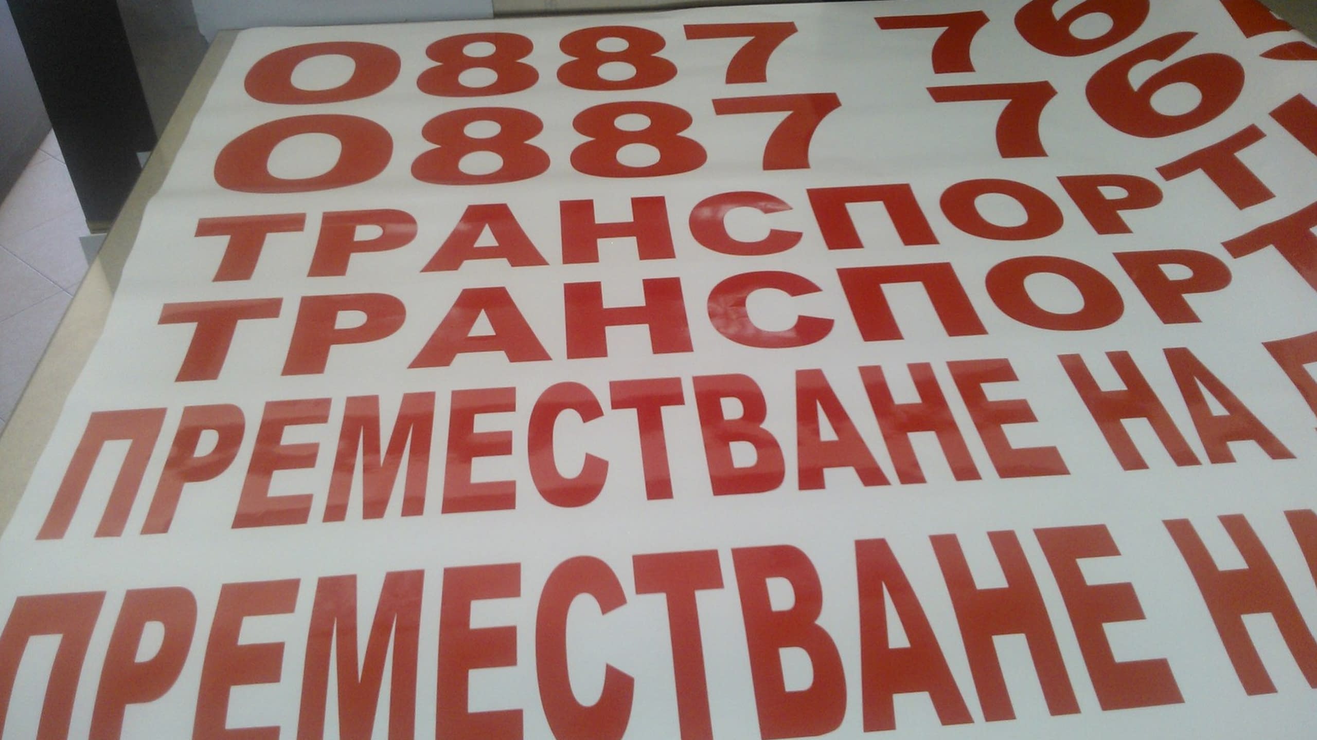 Изрязани на плотер надписи от червено фолио за брандиране на камиони на транспортна фирма.