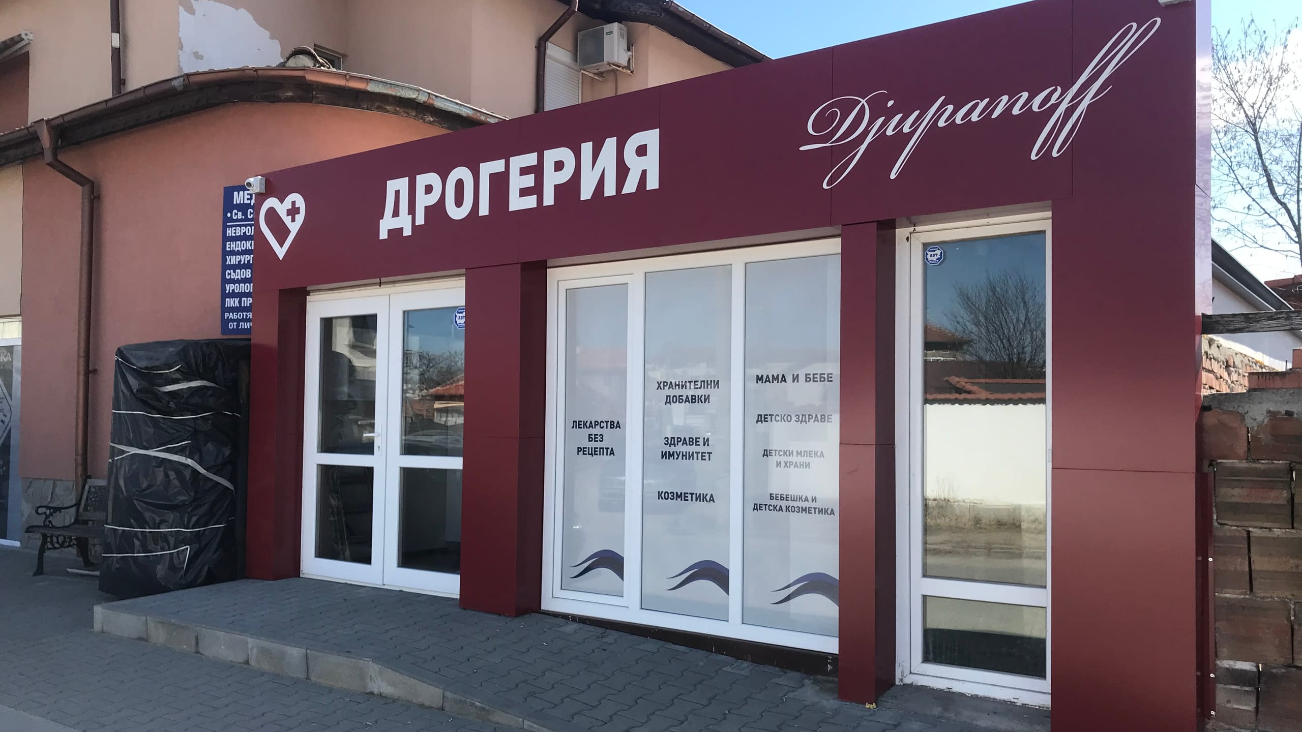 Цялостно брандиране на дрогерия "Djuranoff" с голяма рекламна табела и надписи от бяло фолио върху витрините, изброяващи категории продукти.